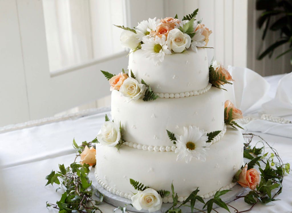 Elegant white wedding cake adorned with fresh roses and daisies, perfect for a romantic celebration.